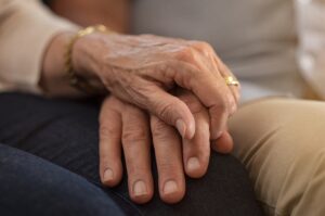 Closeup of elderly couple holding hands while sitting on couch.